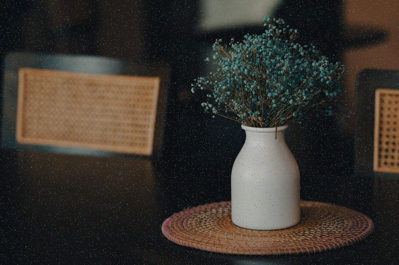A white ceramic vase of dried baby's breath on a woven mat, in a dim interior.