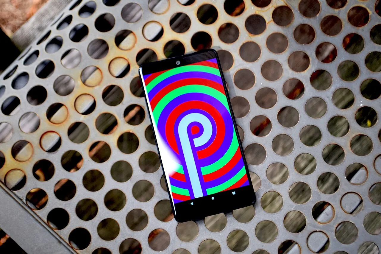 An Essential Phone on a metal bench showing the Android 9 Easter egg: a large letter P over red, green and purple rings, with the display cutout at the top